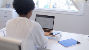 Small business cyber security at a bright office desk, with a person working on a laptop beside a phone and tablet